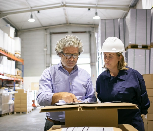 Oracle RMS website section for manufacturing key professions featuring a supervisor in a hard hat and an advisor inspecting items in a cardboard box within a warehouse environment.